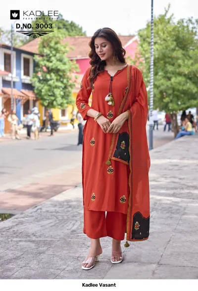Kadlee Vasant Vol 3003, orange salwar suit featuring floral thread work, tassels, and a contrasting panel on the dupatta, worn outdoors.