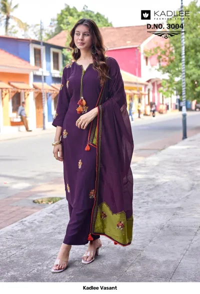 Kadlee Vasant Vol 3004, deep purple salwar suit with floral thread work, tassels, and a green-bordered dupatta, worn outdoors.