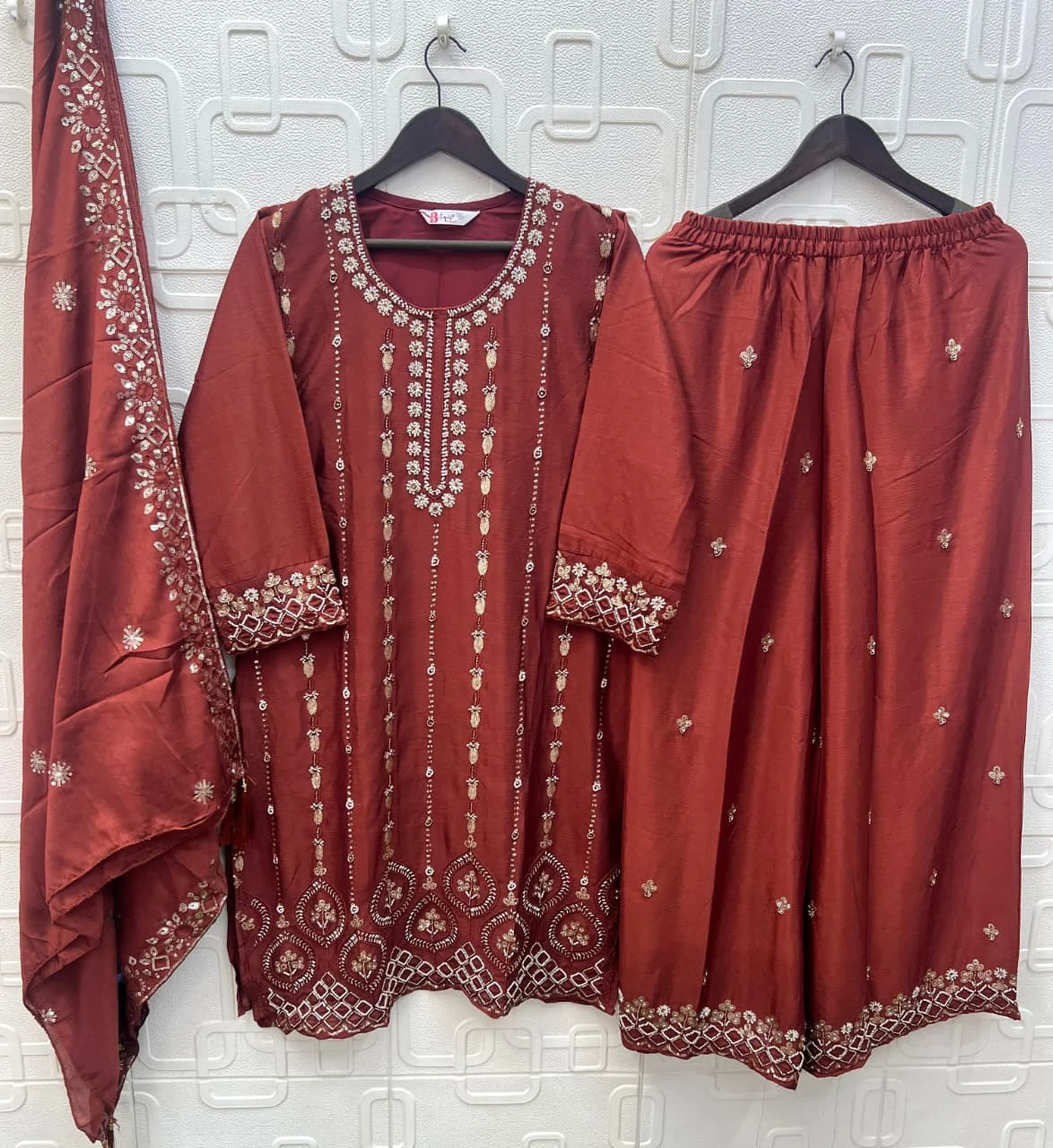 Bilqis B 271 ABCD: A rust-colored salwar suit with a kurta and wide-leg palazzo, featuring silver thread work embroidery and embellishments on the borders.