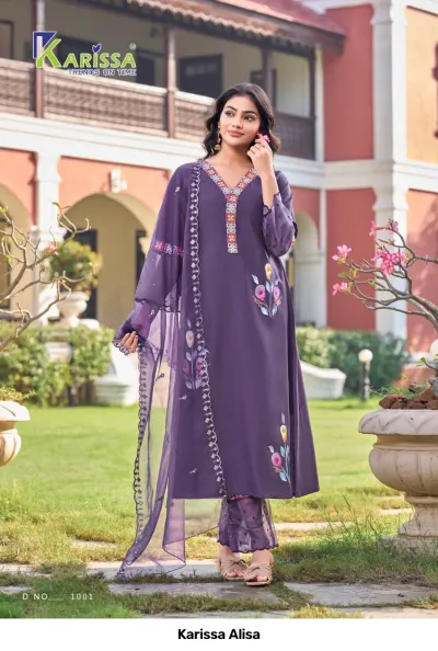 Karissa Alisa purple salwar suit with floral printed motifs, v-neckline, and matching dupatta, worn by a model standing outdoors.