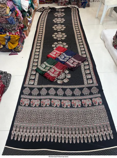 Wholesale Ajrak Printed Crepe Sarees: Catalog layout displaying a black saree with elephant and circular Ajrak prints and folded textile samples.