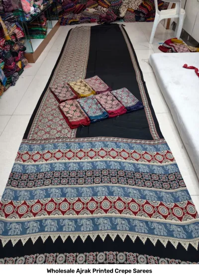 Wholesale Ajrak Printed Crepe Sarees: Seven colorful folded sarees with consistent ornamental Ajrak block print borders.