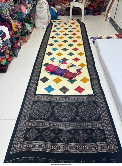 Wholesale Ajrak Printed Crepe Sarees: Catalog layout featuring a white saree with geometric shapes and circular patterns alongside fabric samples.